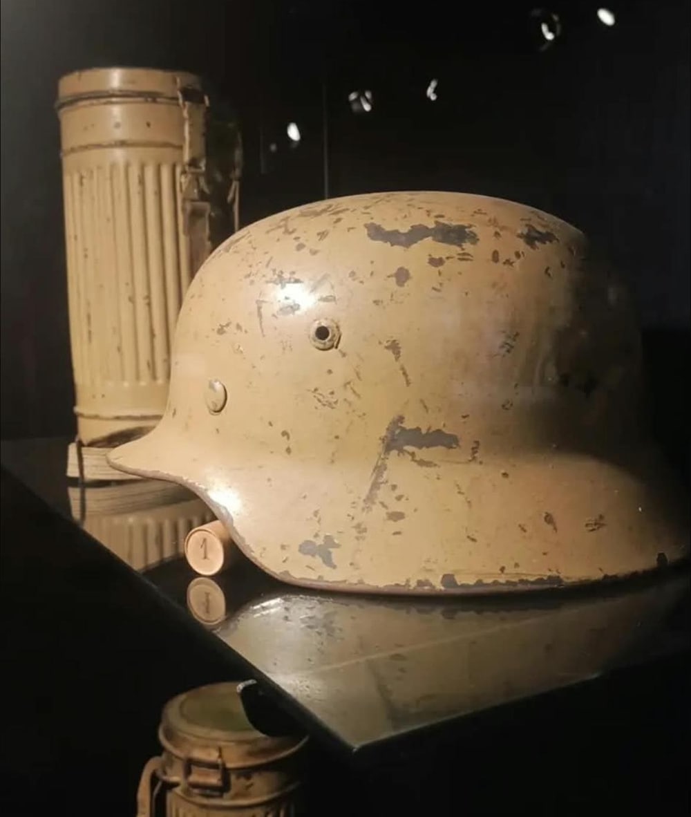 Casco M40 con la pintura de arena del Afrikakorps, saltada hasta el acero. Detrás, el bote de la máscara antigás.