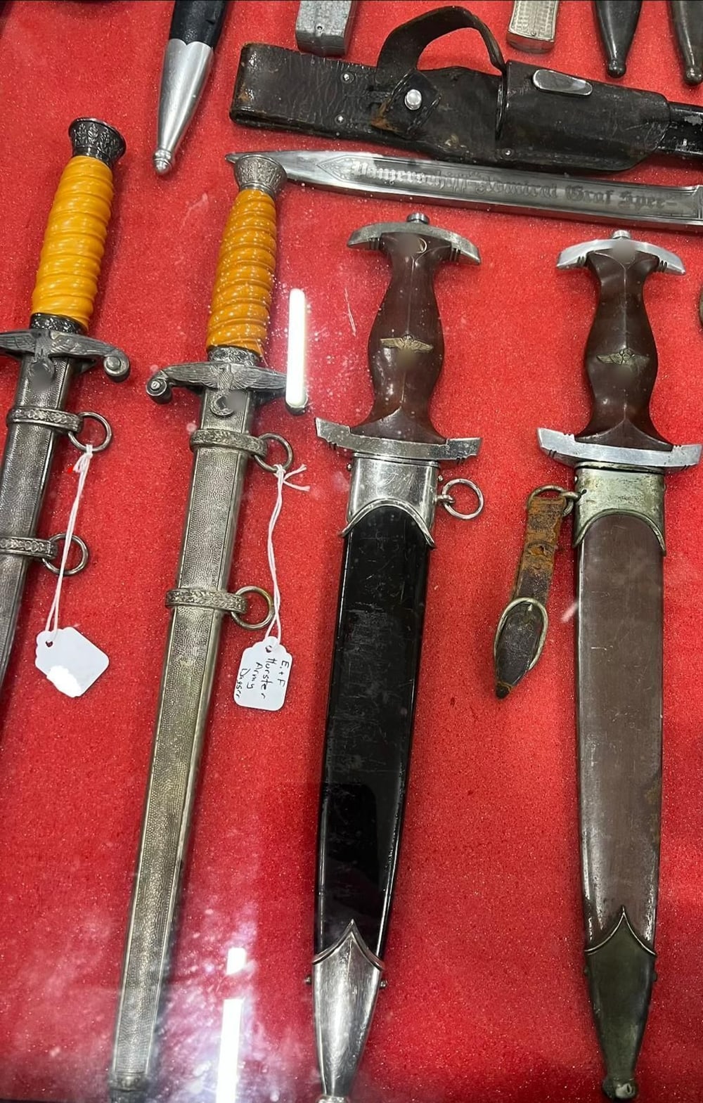 Dos dagas de oficial del Heer con empuñadura naranja y dos dagas de las SA con su vaina. Los símbolos de las empuñaduras van tapados (§ 86a StGB).