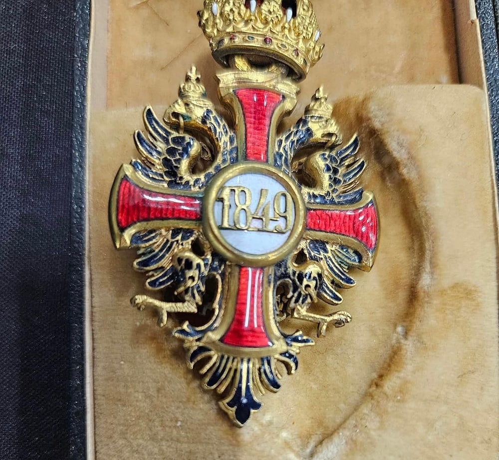 Detalle de la cruz de la Orden de Francisco José: esmalte rojo, águila bicéfala y la fecha de fundación, 1849, en el medallón. En su estuche.
