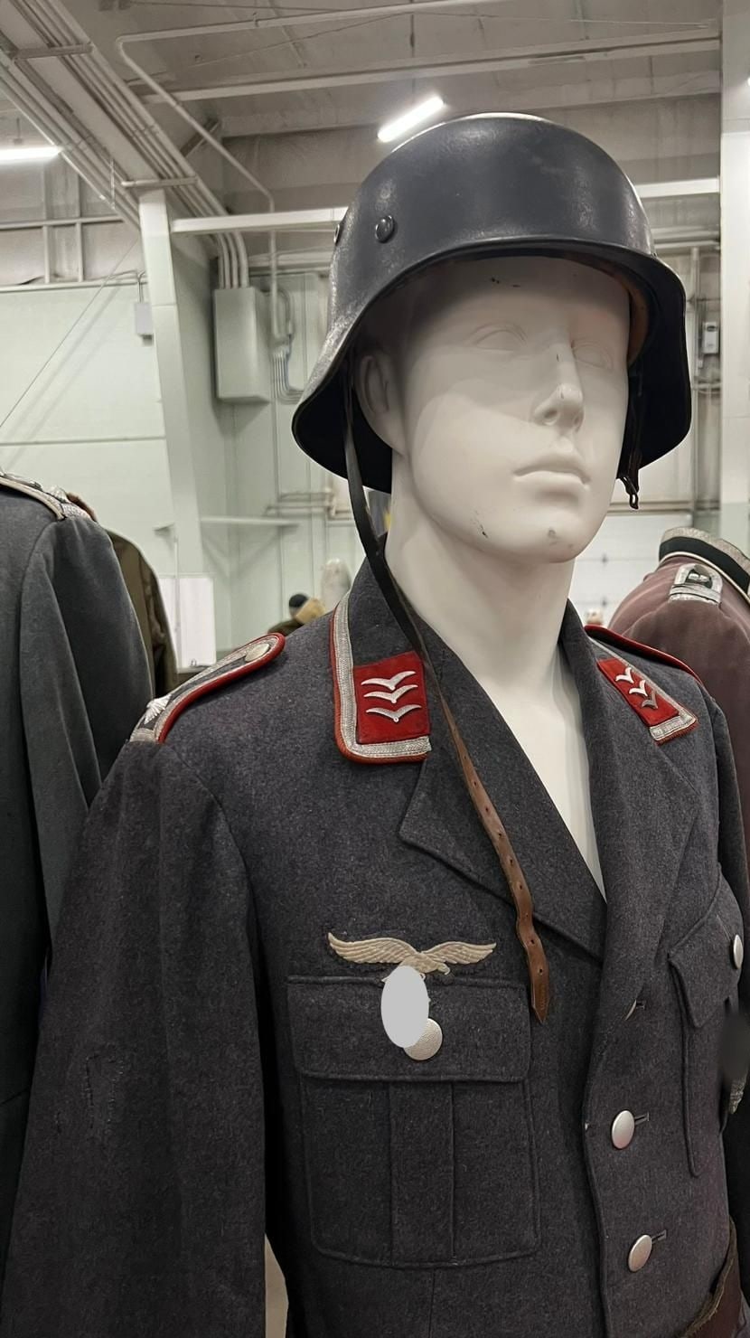 Uniforme de la Luftwaffe en su maniquí: parches de cuello rojos de artillería antiaérea con las alas de rango y casco de acero. El símbolo del águila va tapado (§ 86a StGB).