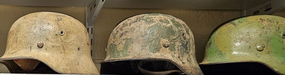 Fila de cascos: arena, camuflaje pintado a mano y verde de fábrica.